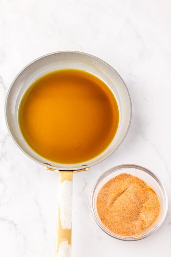A saucepan filled with melted butter next to a small glass bowl containing a pile of taco seasoning on a white surface.