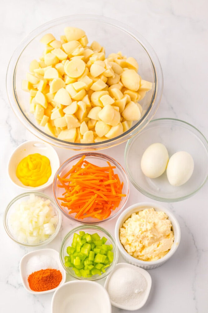 A variety of ingredients for potato salad, including chopped potatoes, two boiled eggs, carrots, mustard, chopped onion, chopped celery, mayonnaise, salt, sugar, and paprika.