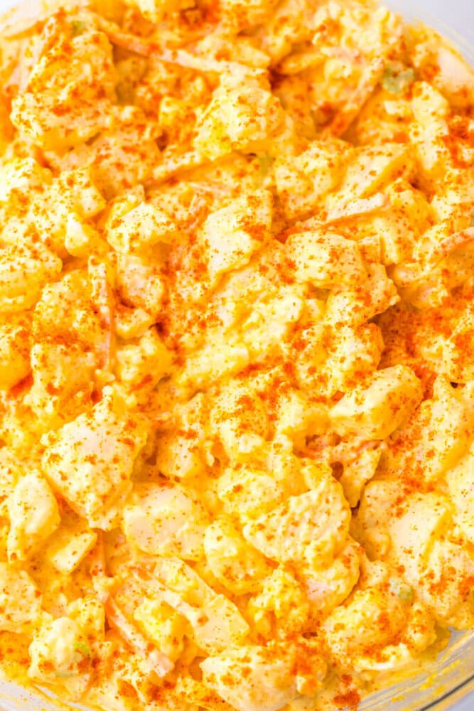 Close-up of classic potato salad mixed with mayonnaise, chopped eggs, and topped with a sprinkle of paprika.