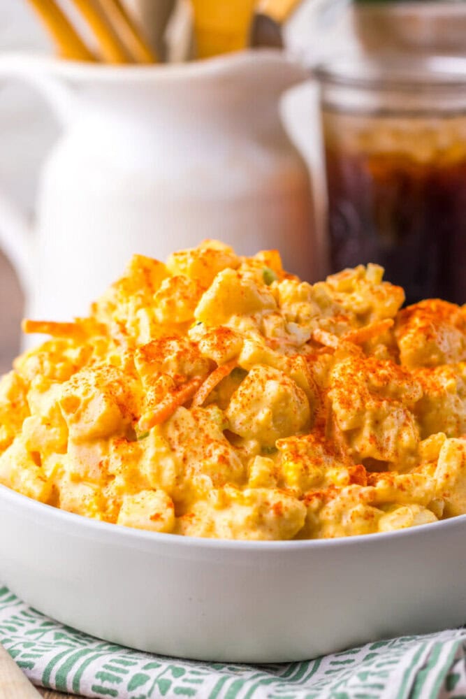 A white bowl filled with creamy macaroni and cheese, topped with shredded cheese and sprinkled with paprika.