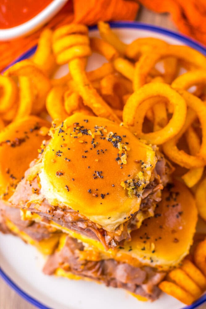 A plate with curly fries and three roast beef sliders on poppy seed-topped buns.