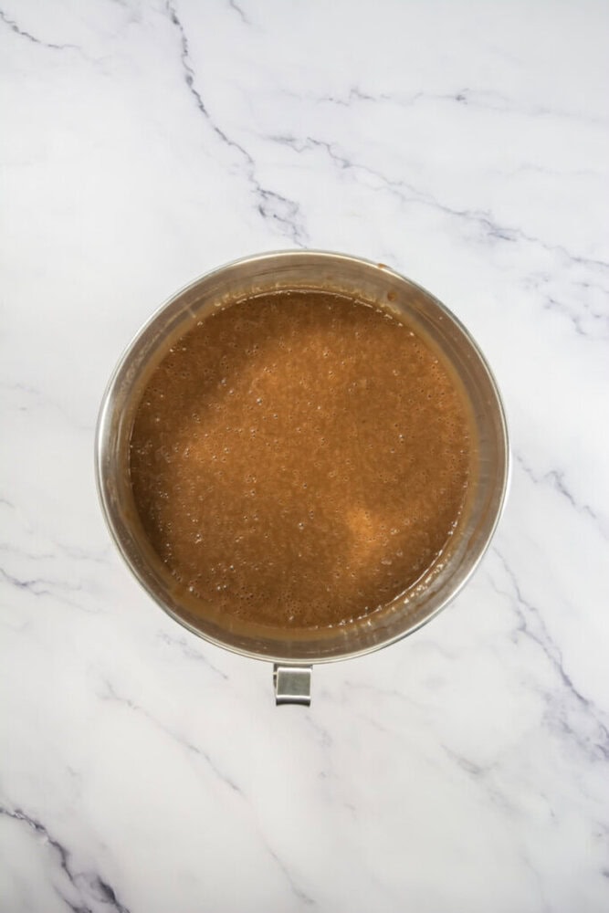 A metal mixing bowl filled with light brown liquid sits on a white marble surface.