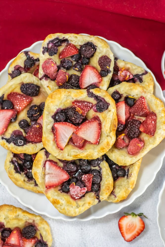 A plate of square puff pastries topped with mixed berries, including strawberries, blueberries, and blackberries, on a white dish.