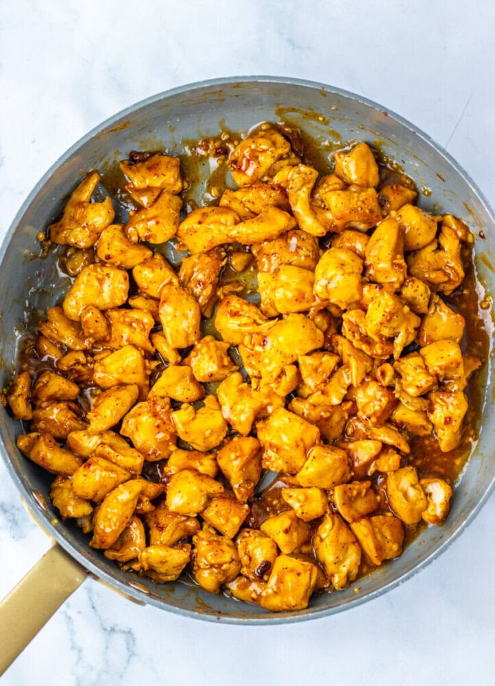 Cooked, bite-sized pieces of seasoned chicken in a nonstick skillet on a marble countertop.