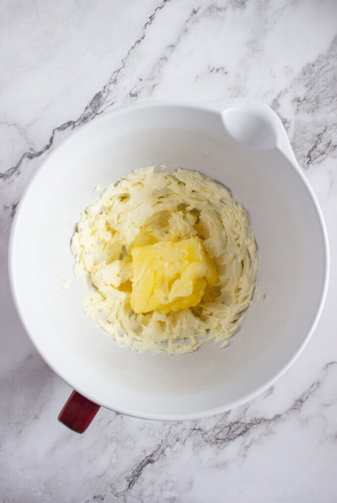 A white mixing bowl containing creamed butter and sugar on a marble countertop.