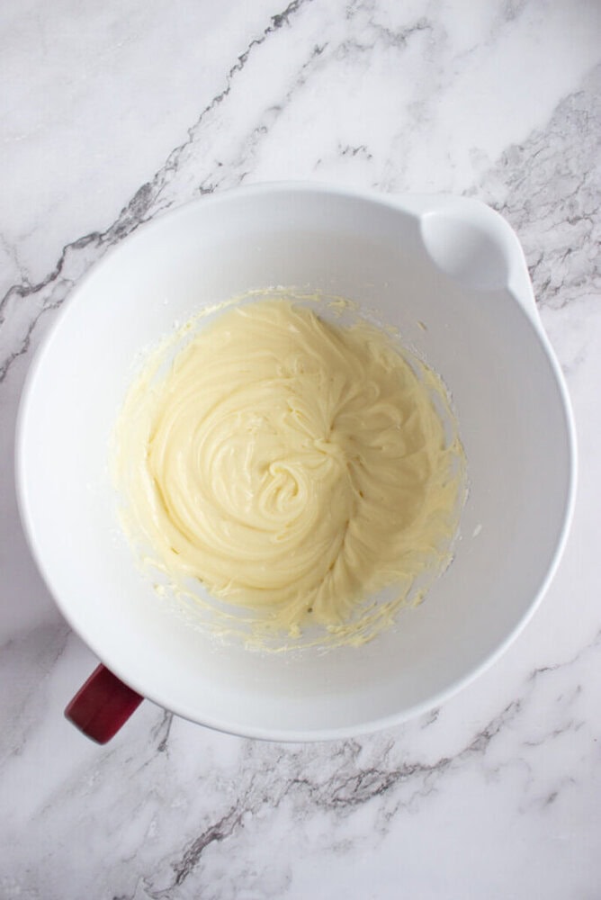 A mixing bowl containing smooth, pale yellow batter sits on a marbled countertop.