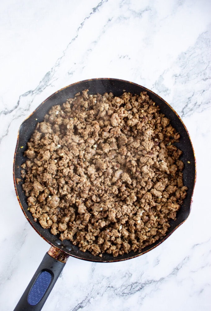 Cooked ground beef in a black skillet on a white marble countertop, viewed from above.