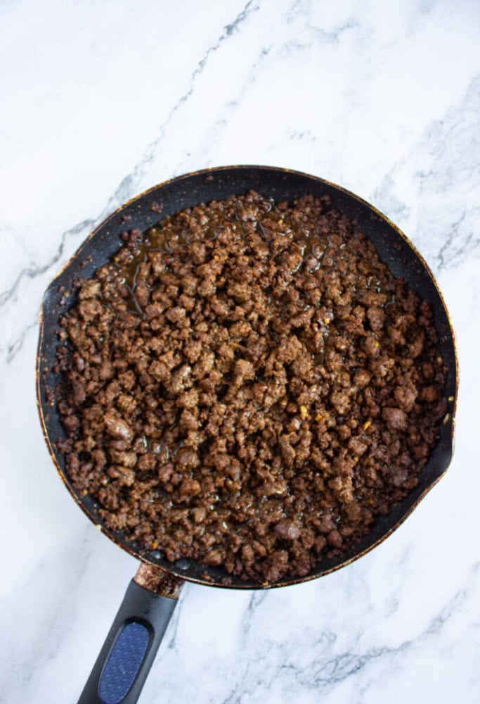 Cooked ground beef in a nonstick skillet on a white marble surface.