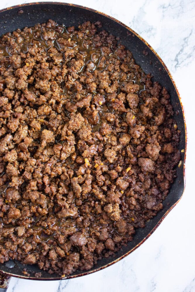 Cooked and seasoned ground beef in a black skillet on a white marble surface.