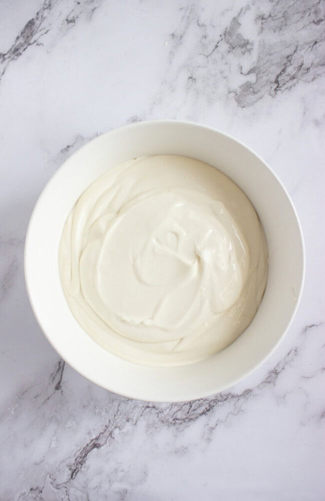 A white bowl filled with smooth, creamy white yogurt sits on a light gray marble surface.