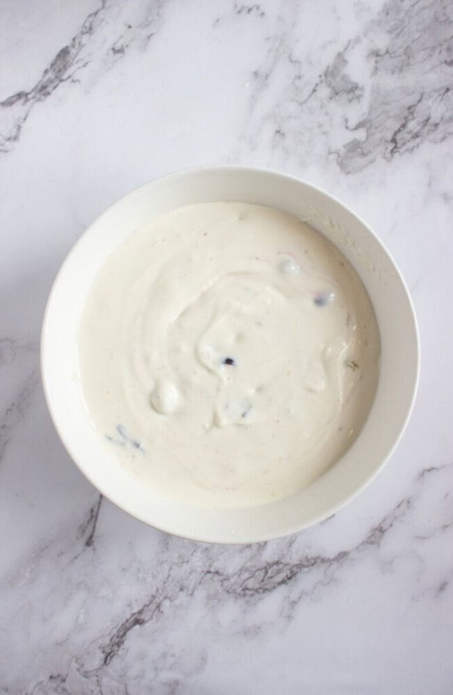 A white bowl filled with thick, creamy yogurt sits on a light marble surface.