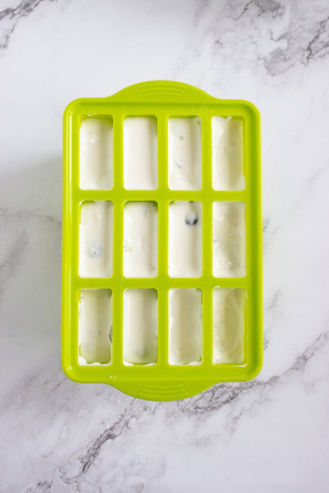 A green silicone mold tray filled with a white creamy mixture, resting on a white marble surface.