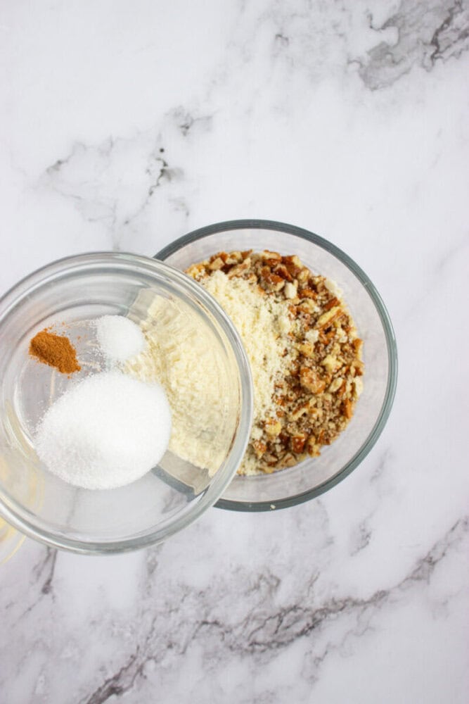 Two glass bowls on a marble surface; one bowl contains sugar, salt, and cinnamon, while the other holds chopped nuts and flour.