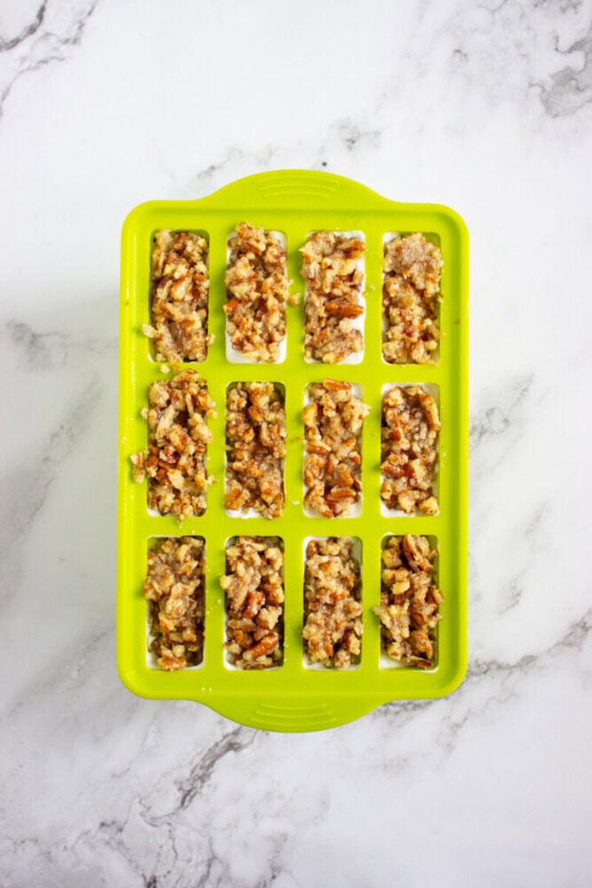 A green silicone mold with twelve rectangular cavities filled with a chunky mixture sits on a white marble surface.