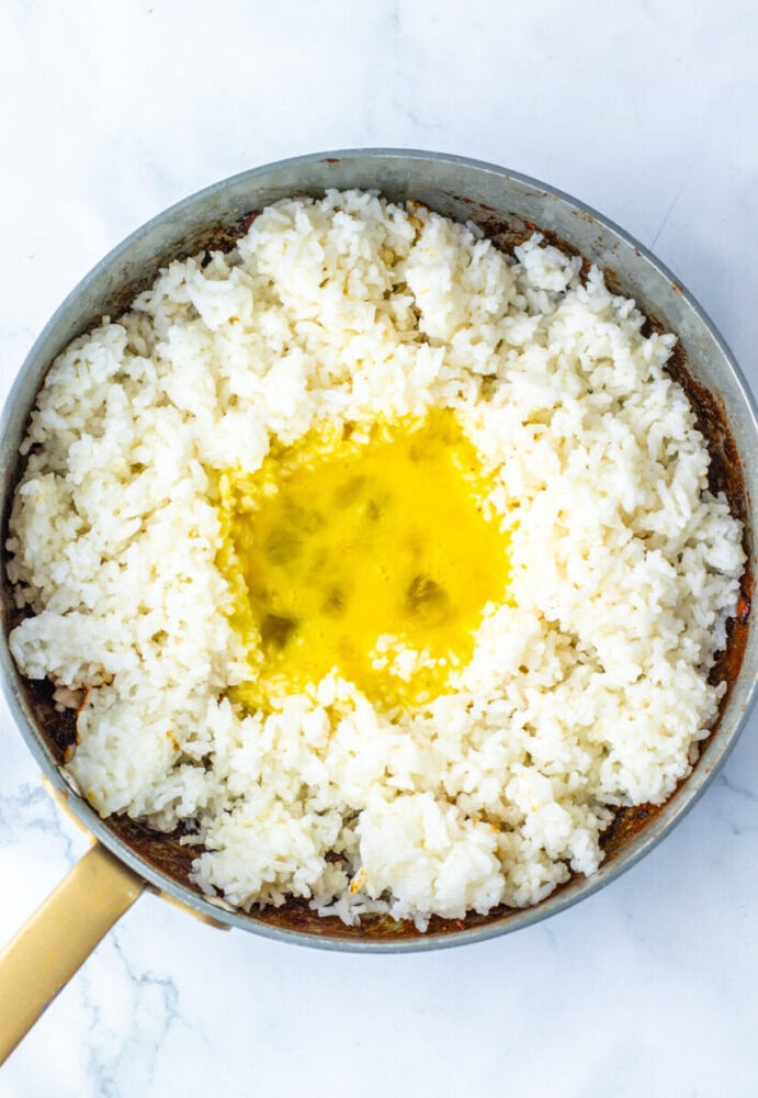 A pan filled with cooked white rice arranged in a ring, with raw beaten egg poured into the center.