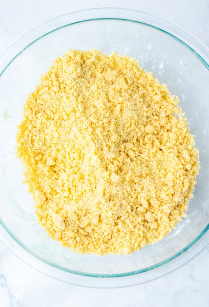 A glass bowl filled with coarse, yellow crumbly mixture sits on a white surface.