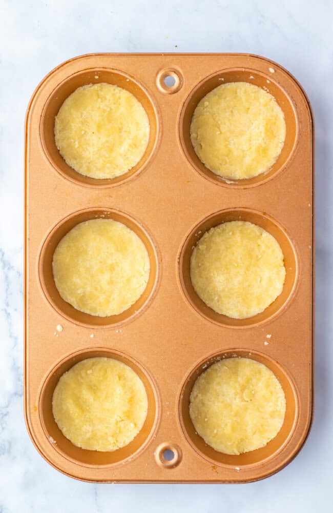 A muffin tin with six unbaked, round dough balls placed in each cup, set on a light marble surface.