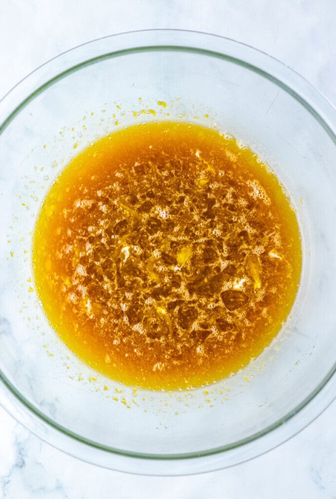 A glass mixing bowl filled with melted butter and brown sugar combined, resting on a white surface.