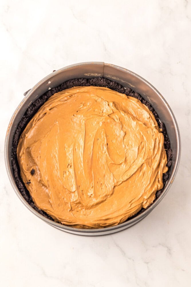 A round cake pan filled with an Oreo cookie crust and topped with a smooth, thick layer of peanut butter filling.
