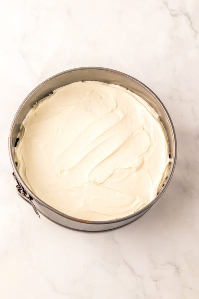 A round springform pan filled with smooth, spread, creamy cheesecake batter on a white marble surface.