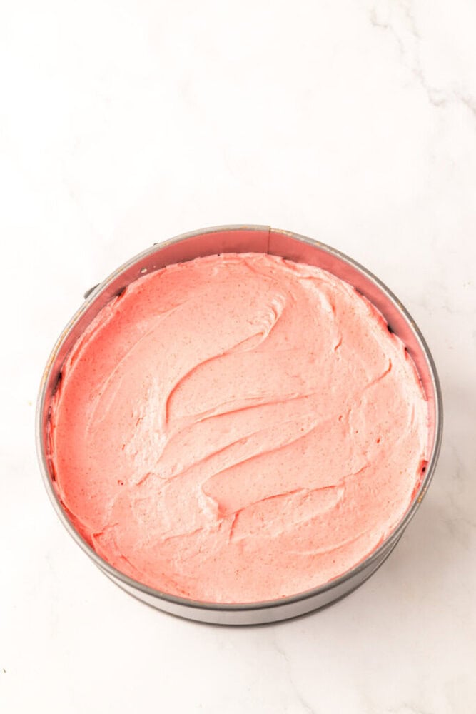 A round springform pan filled with smooth, pink cake batter on a white marble surface.