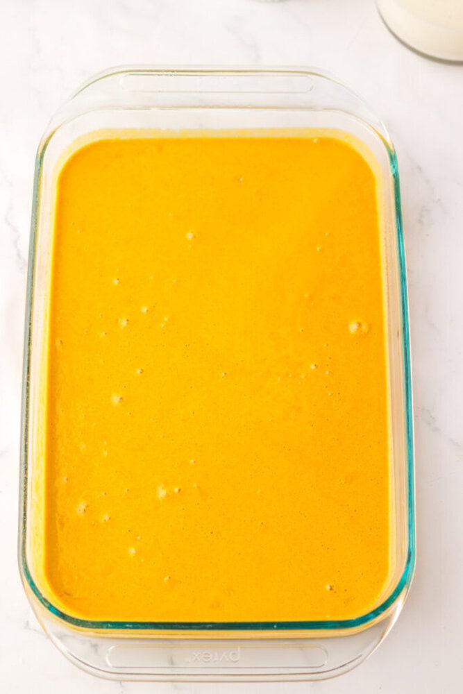 A glass baking dish filled with a smooth, bright orange liquid mixture, set on a white surface.