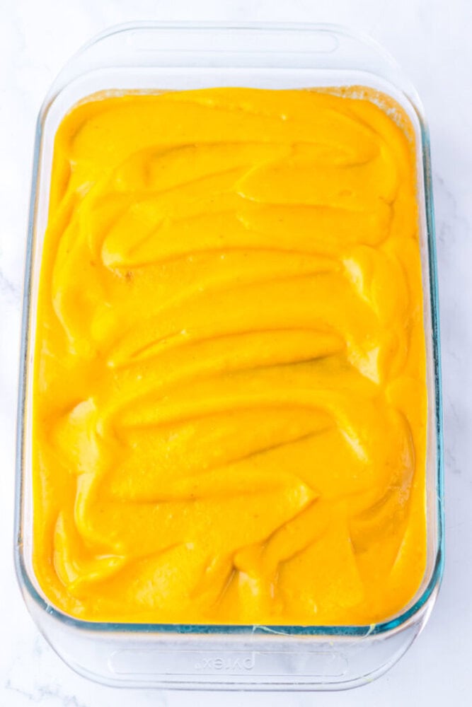 A glass baking dish filled with a smooth layer of bright yellow-orange puree, evenly spread across the top.