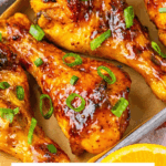 Orange Glazed Chicken legs, garnished with green onions, sit on a baking tray ready to serve&mdash;perfectly roasted chicken legs with a glossy, flavorful glaze.