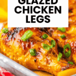 Close-up of roasted chicken legs glazed with orange, garnished with green onions on a metal tray.