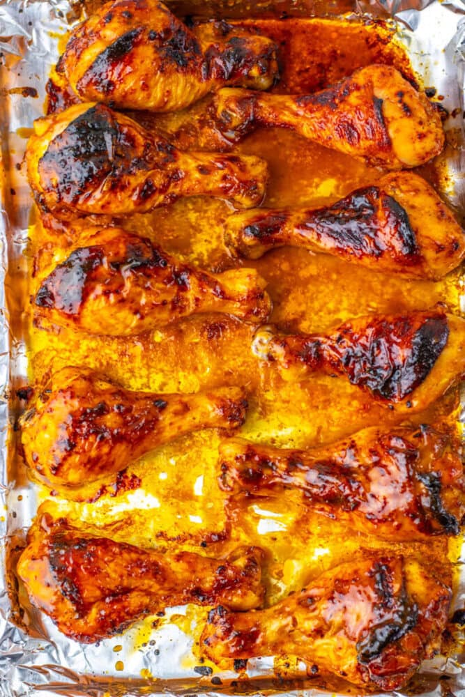 Baked chicken drumsticks with a glazed, slightly charred coating arranged on a foil-lined baking sheet.