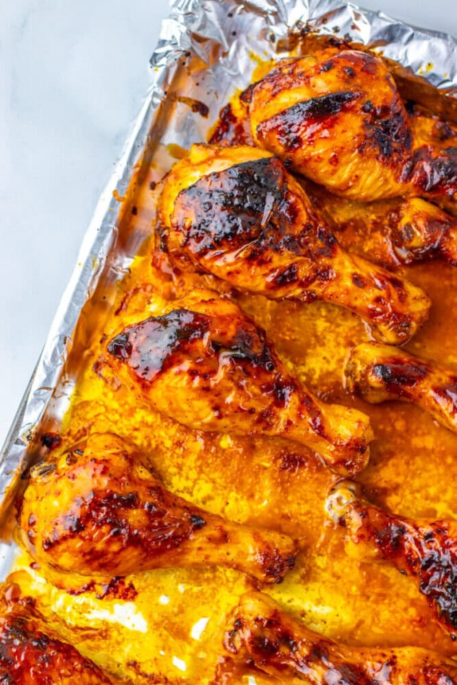 Baked chicken drumsticks coated in a glossy, orange-brown sauce on a foil-lined baking sheet.