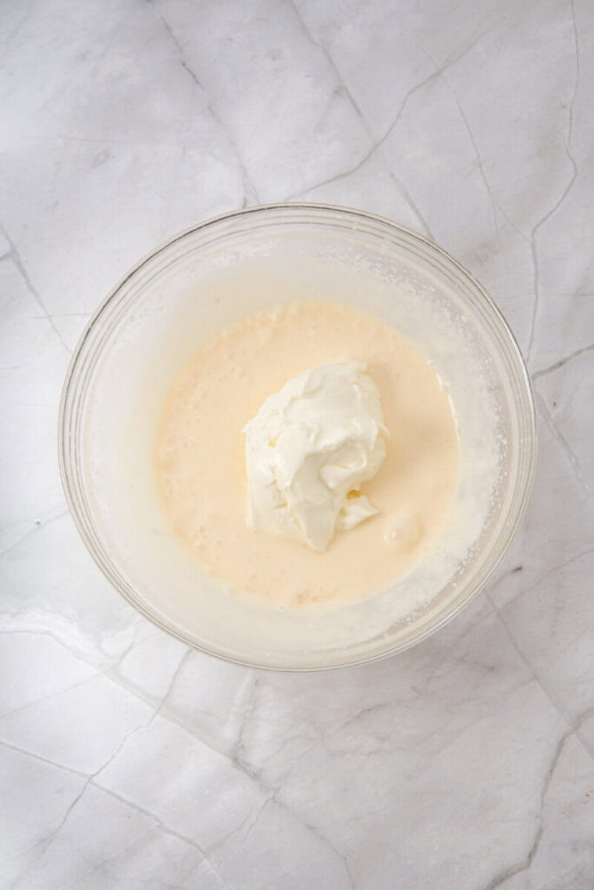 A glass bowl containing a mixture of white liquid and a dollop of thick white cream sits on a marble surface.