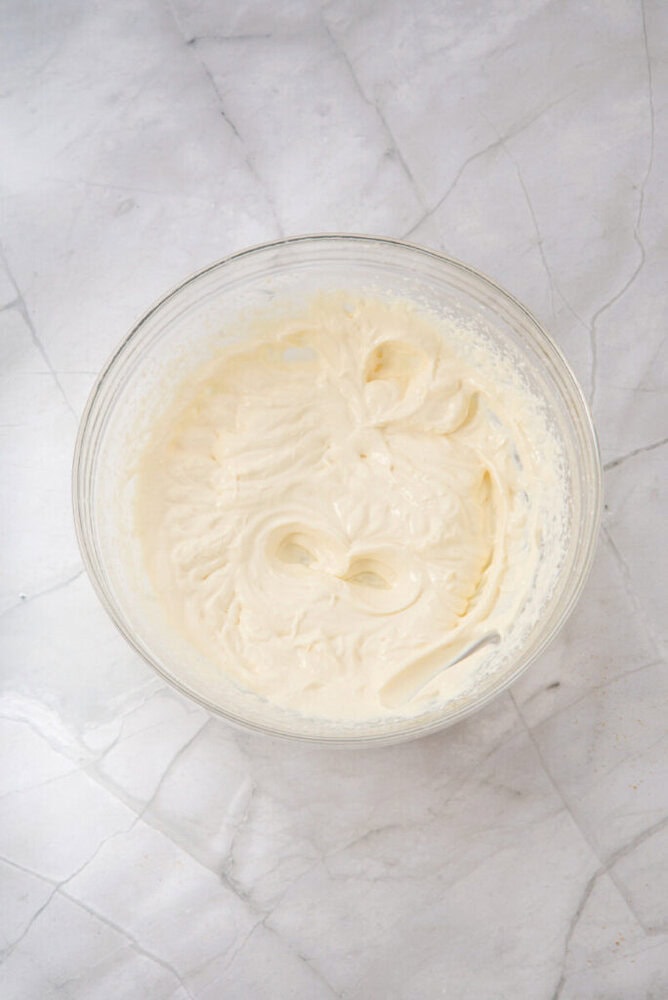 A glass bowl filled with thick, whipped cream sits on a white marble surface.