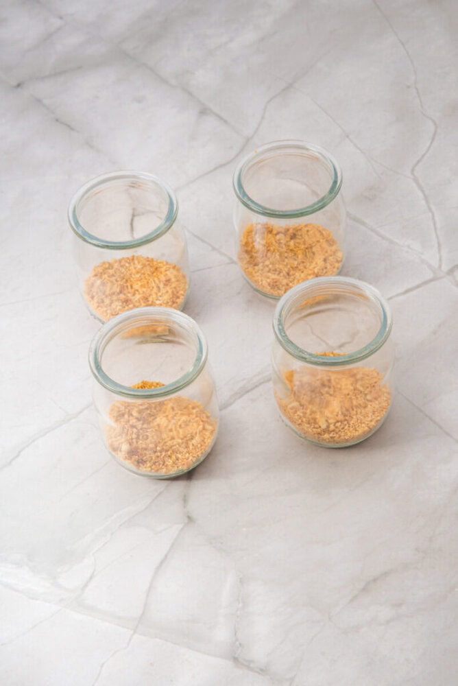 Four small glass jars each containing a portion of dry oatmeal are arranged on a light gray marble surface.