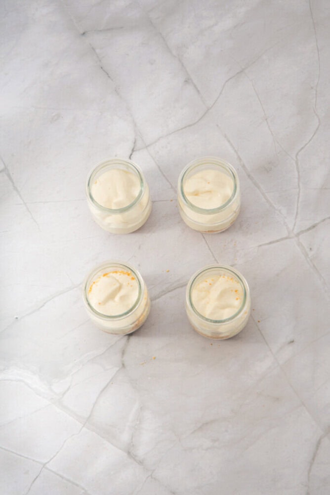 Four small glass jars containing a creamy dessert are arranged in a square on a light marble surface.
