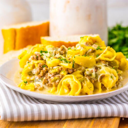 A plate of creamy tortellini pasta with ground meat and herbs, served with slices of bread, on a striped napkin.