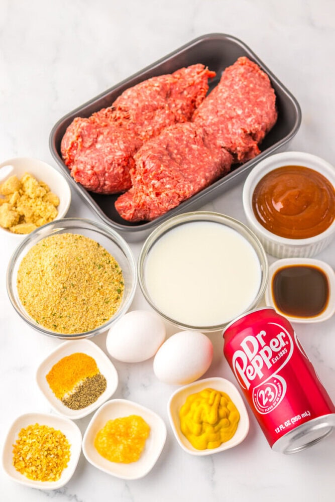 Various ingredients for cooking, including ground beef, eggs, bread crumbs, spices, milk, mustard, Worcestershire sauce, barbecue sauce, brown sugar, and a can of Dr. Pepper, are arranged on a counter.