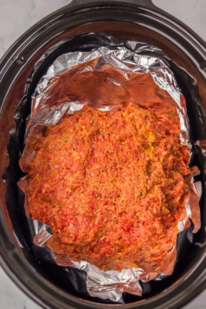 Raw meatloaf mixture placed on aluminum foil inside a slow cooker, ready to be cooked.