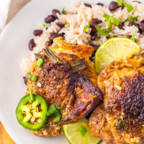 A plate with seasoned roasted chicken thighs, lime slices, jalapeño slices, and a side of rice mixed with black beans.