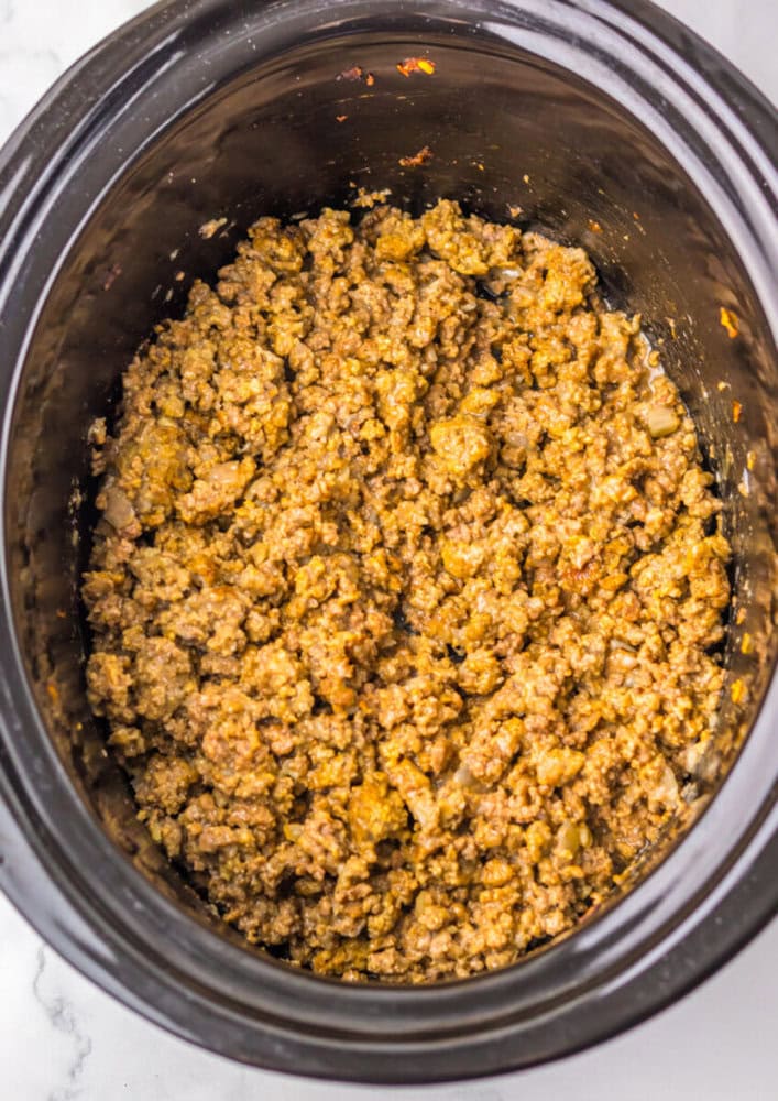 Cooked ground meat mixed with seasonings is shown in a black slow cooker, viewed from above.