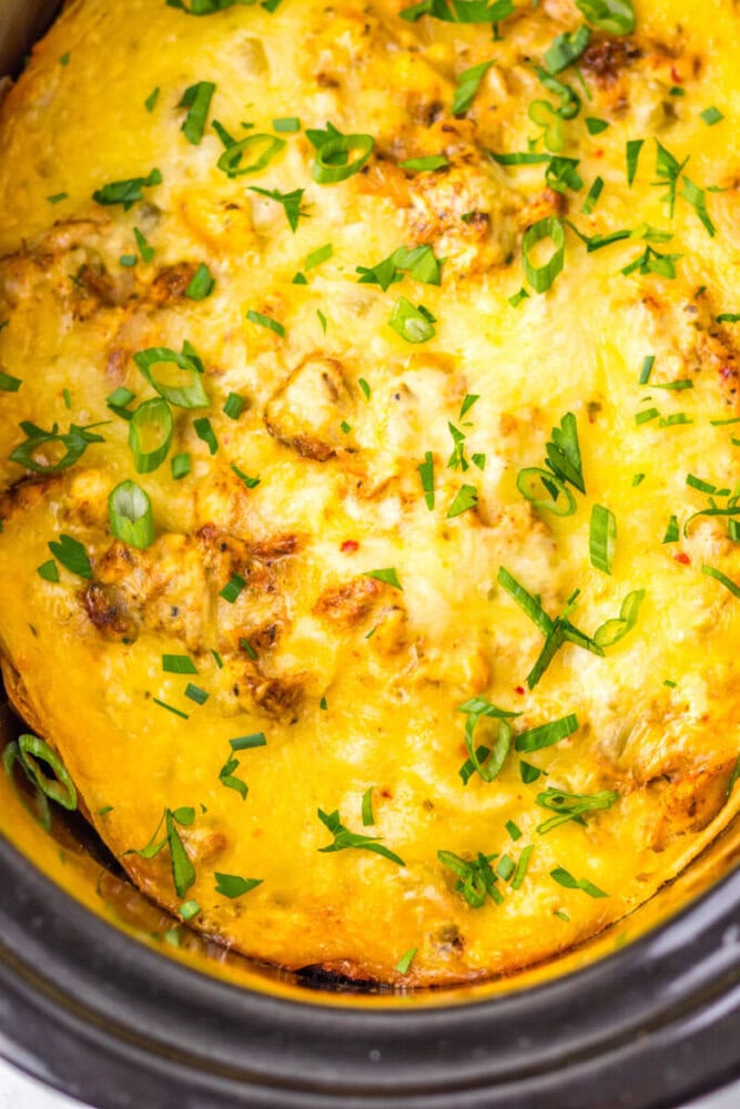 Close-up of a cheesy casserole topped with chopped green onions and herbs, baked in a slow cooker.