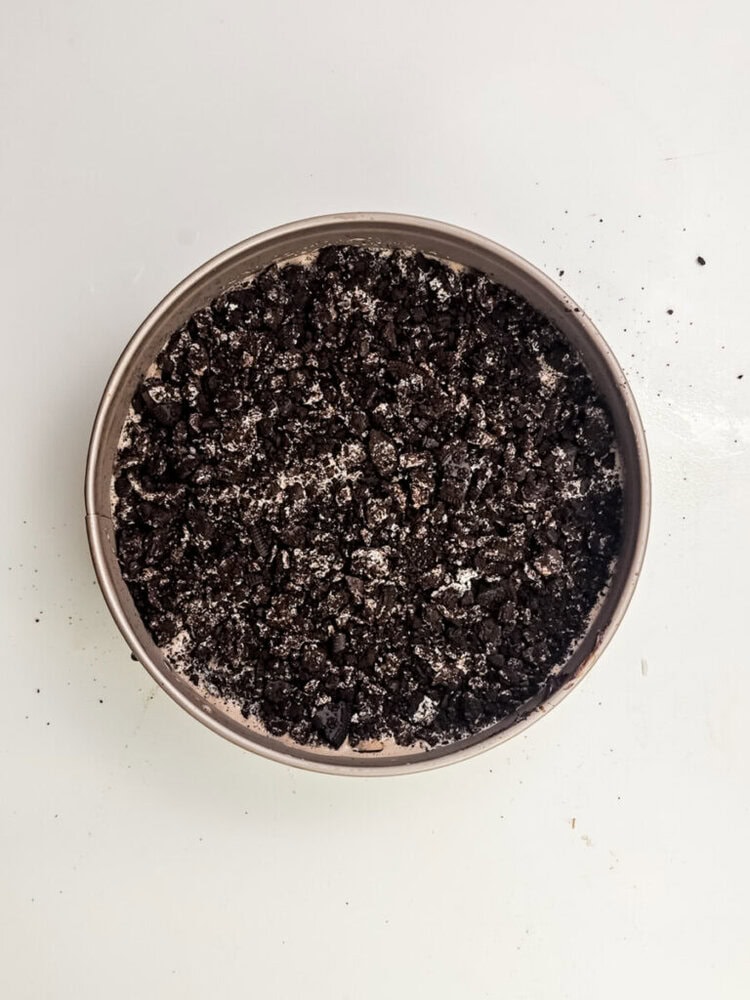 A round tin filled with crushed chocolate cookies on a white surface.