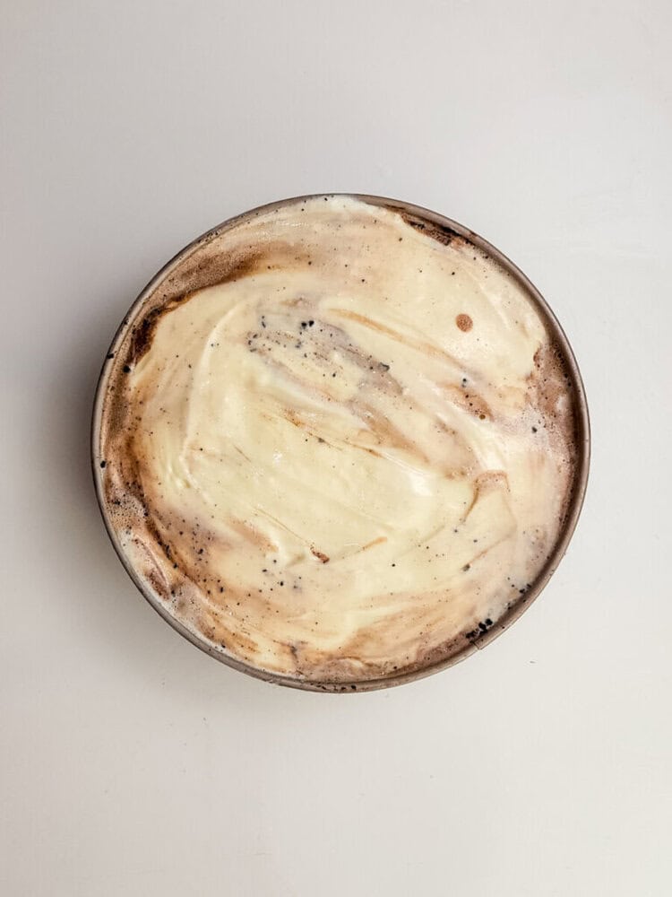 A round bowl filled with a creamy dessert featuring swirled layers of white and brown on a plain light surface.