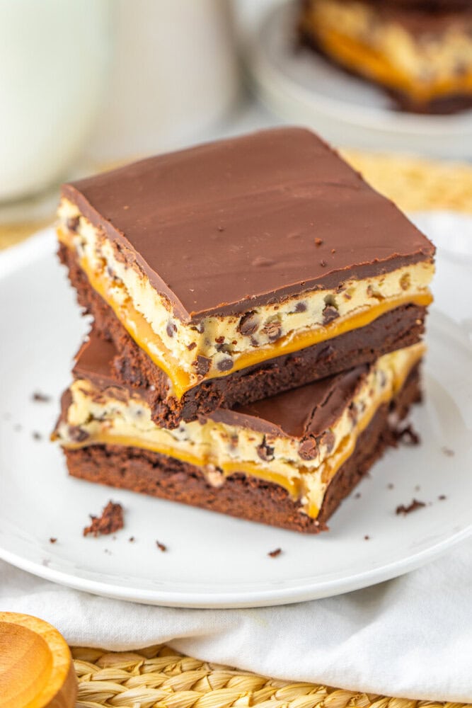 Two stacked chocolate layered dessert bars with a cookie dough center and chocolate chips, displayed on a white plate.