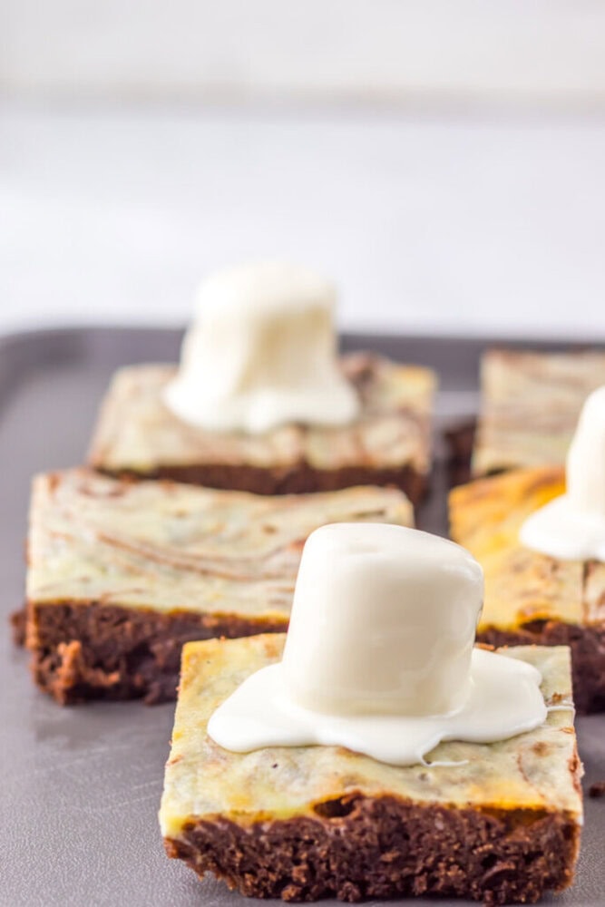Four square brownie bars topped with a melted marshmallow and white chocolate coating, arranged on a baking tray.