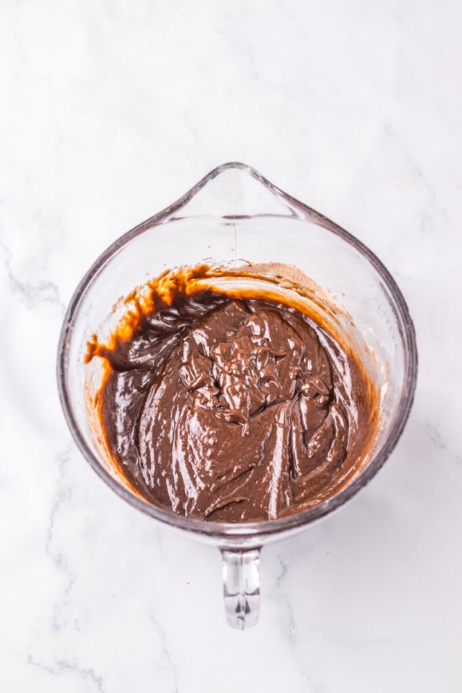 A glass mixing bowl filled with chocolate batter, resting on a white marble surface.