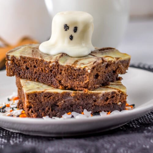 Two marbled brownies stacked on a plate, topped with a white chocolate ghost decoration and surrounded by festive sprinkles.