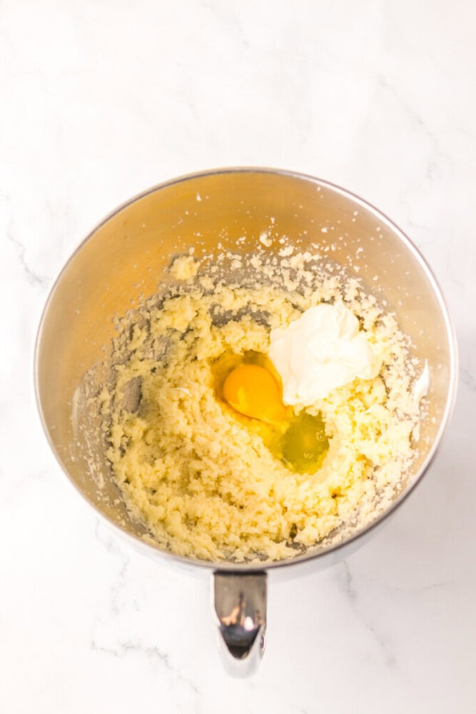 A mixing bowl containing creamed butter and sugar with an egg and cream cheese added on top, ready to be mixed further.