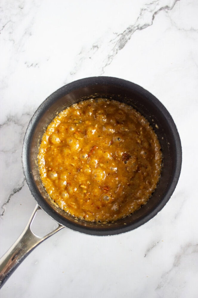 A saucepan containing a bubbling caramel sauce sits on a white marble surface.