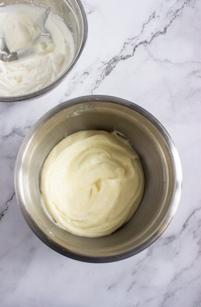 Two metal bowls sit on a marble surface, each containing a creamy white mixture, with one bowl positioned near the top left corner and the other in the center.